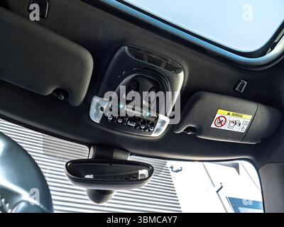 Paris, France - Mar 27, 2025: Interior view of a MINI electric car showing the roof console with toggle switches, dome light, emergency call button, and sun visors with airbag warning label and mirror. Stock Photo