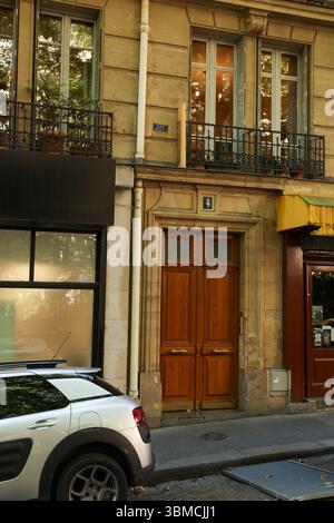 A charming Parisian street scene featuring a silver car parked near a building with an elegant brown wooden door. Stock Photo