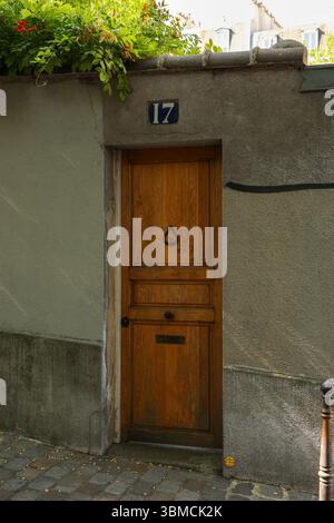 A photograph of an aged, rustic wooden door on a building in Paris. The door is brown with a simple design and features a classic door knocker. Above Stock Photo