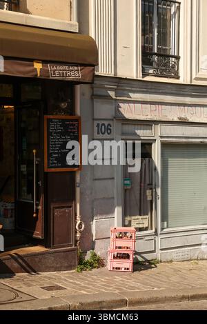 A charming Parisian street scene featuring a cafe with a chalkboard menu, two pink crates filled with bottles, and a vintage building facade with weat Stock Photo