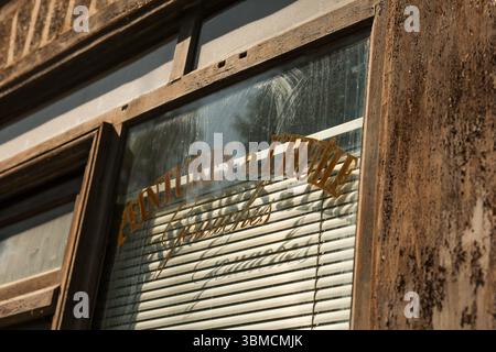 Close-up shot of a weathered wooden window frame of an old shop. A faded gold sign reading 'Peintures a l'Huile' is visible on the dusty glass, behind Stock Photo