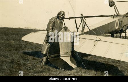 Original WW1 era plane with a cheerful looking pilot possibly of the Royal Flying Corps (RFC) in flying gear including a long leather trench coat, leather cap and gloves, standing next to his upside down plane, which has flipped over and crashed - he is holding the broken tail and grinning. 1914-1918 Stock Photo