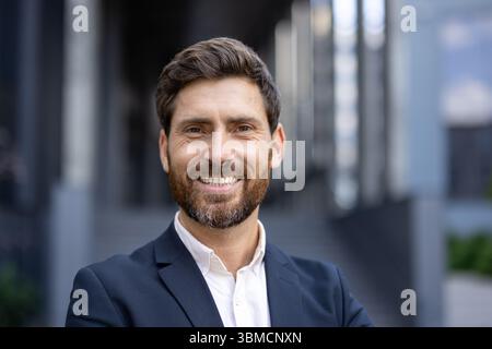 A smiling businessman in a suit, outdoors, with a building in the background. Stock Photo