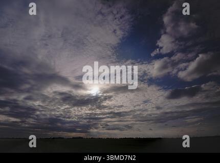 Dark clouds in the sky with sun in the backlight, on the horizon high-voltage pylons with power lines behind a field, Braunschweig, Lower Saxony, Germ Stock Photo