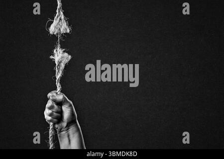 Hold on to Frayed Rope About to Break Against Textured Black Paper Background with Copy Space Stock Photo