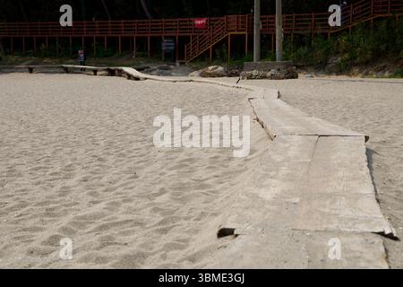 Samcheok City, South Korea - May 31st 2025: A well-worn set of wooden planks cuts across the soft sand of Deoksan Beach, guiding visitors toward the f Stock Photo