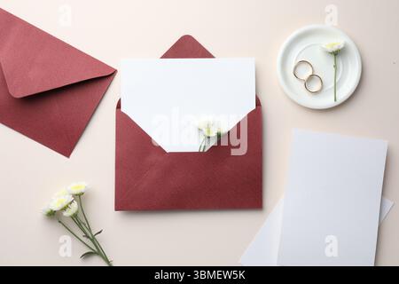 Wedding invitation cards, envelopes, gold rings and flowers on beige background, flat lay Stock Photo