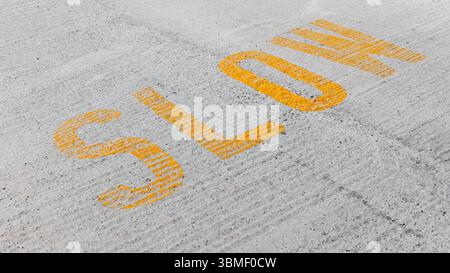 Yellow text reading SLOW painted on a textured asphalt surface for road safety and traffic management. The image emphasizes caution and careful drivin Stock Photo