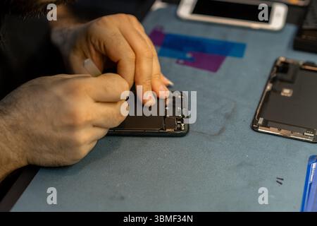 Expert Technician Repairs Smartphone Screen With Precision in a Busy Repair Shop During the Afternoon Hours Stock Photo