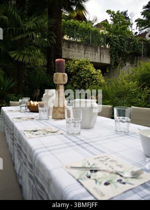 Rustic outdoor table set in a green garden with vintage candle holders, glassware, and patterned tablecloth for a peaceful gathering. Stock Photo