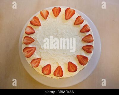 Overhead shot of a strawberry cake with whipped cream and halved strawberries arranged in a circle on top. Stock Photo
