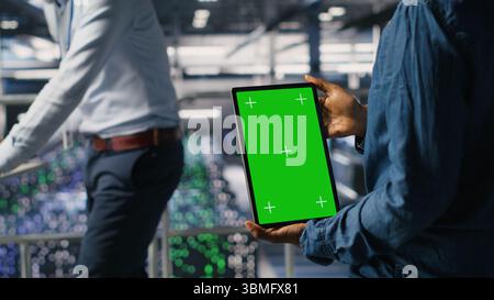 Data center engineers monitoring neural network LLM visualization using green screen tablet. Server farm IT experts oversee rigs powering machine learning processes using chroma key device Stock Photo