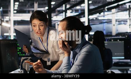 Programmers doing brainstorming in server room, reviewing neural network code and LLM visualization dashboards. Data center coworkers monitoring artificial intelligence systems performance, camera A Stock Photo
