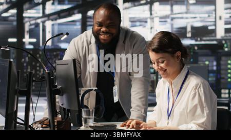 Joyous data center team leader giving high five to worker after successful infrastructure upgrade. Pleased coworkers celebrating collaborative achievement during AI systems deployment, camera A Stock Photo