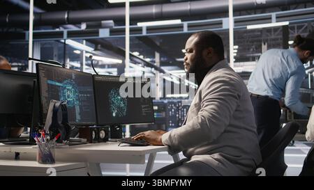 Exhausted server farm employee stretching back after sitting too long at computer desk. Fatigued man in data center office relaxing muscles, stressed by long hardware troubleshooting session, camera A Stock Photo