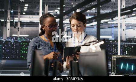 Data center teamworking colleagues performing maintenance on server racks used for artificial intelligence processing. Engineering team managing server hub rigs used for machine learning, camera A Stock Photo