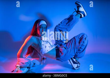 A woman is doing a dance move in front of a blue background. Scene is energetic and fun Stock Photo