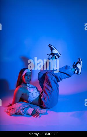 A woman is laying on her back with her legs spread apart and her arms outstretched. She is wearing a white shirt and blue jeans. The image has a cool, Stock Photo