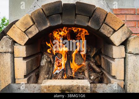 Fire burns brightly in a traditional wood-fired brick oven. An outdoor oven for cooking pizza and bread. Stock Photo