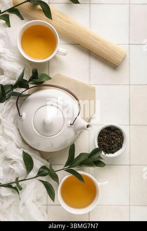 Composition with teapot, bowl with dry leaves and cups of tea on white tile background Stock Photo
