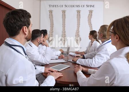 Team of doctors using video projector during conference about scoliosis indoors. Illustrations on projection screen Stock Photo