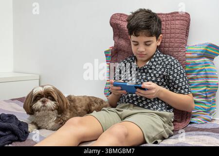 12 year old teenager next to his dog and playing with smartphone. Stock Photo