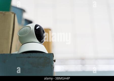 Compact wireless indoor security camera placed high on shelf for enhanced surveillance. Smart technology device for monitoring activity in modern home Stock Photo
