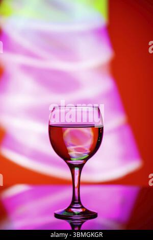 A glass with a drink on a beautiful red background illuminated with colored light Stock Photo