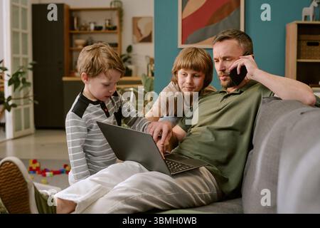 Middle Aged Man Working Remotely While Interacting with Children Stock Photo