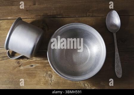 Empty aluminum dish, spoon and overturned mug on the old wooden table Stock Photo