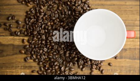 Flat design is showing dark roasted beans and red-handled white coffee cup resting on wood tabletop Stock Photo