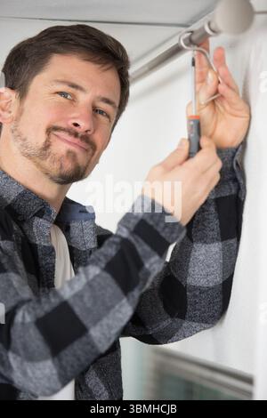 man screwing window curtain rod support on the wall Stock Photo