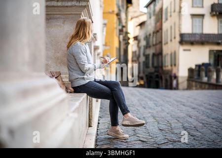 Woman pencil drawing ancient architecture in sketchbook in Bergamo, Italy. Female artist painting during her vacation in Europe Stock Photo