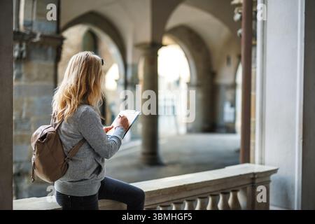 Woman pencil drawing ancient architecture in sketchbook in Bergamo, Italy. Female artist painting during her vacation in Europe Stock Photo