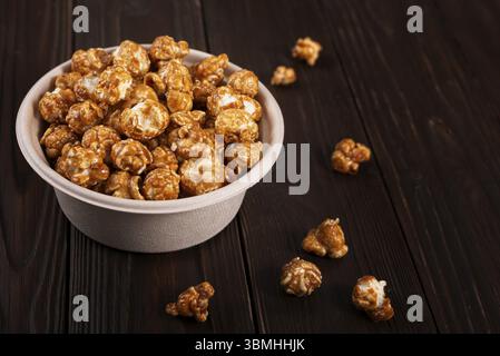Caramelized popcorn in paper bucket on wooden kitchen table Stock Photo