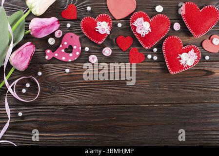 Sewed handmade fabric hearts tulips and ribbon for valentine day on dark wooden background with copy space Stock Photo