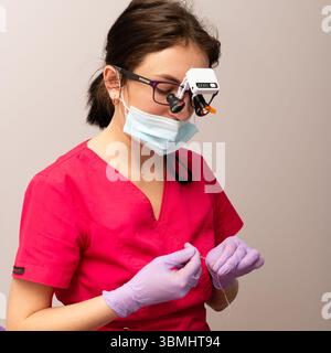 Focused individual in pink medical attire is engaged in a meticulous task, using special equipment to enhance vision while working with fine materials Stock Photo