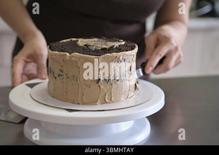 Woman pastry chef making chocolate cake with chocolate cream, close-up. Cake making process, Selective focus Stock Photo