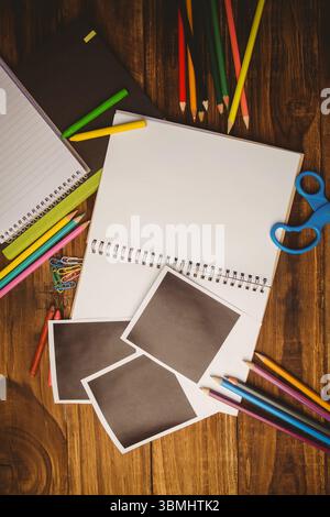 Spiral sketchbook is lying on wooden tabletop in flat design with pencils, scissors, blank prints Stock Photo