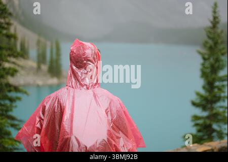 Backview of young man in red plastic poncho at Moraine Lake in Banff Stock Photo