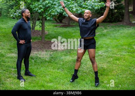 A man doing jumping jacks outdoors under a trainers supervision Stock Photo