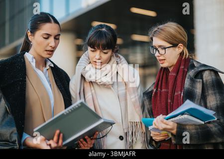 Three professional women collaborating and discussing documents outdoors in business attire Stock Photo