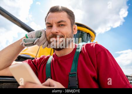 Smiling man combine operator using smartphone near combine harvester Stock Photo