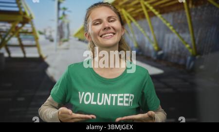 Woman wearing a shirt is pointing in a studio at volunteer blonde young wearing a tshirt and green earring. Stock Photo