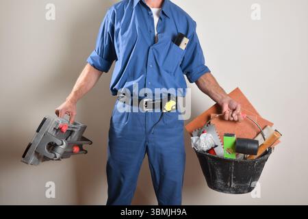 Smiling tiler with ok gesture showing tools and materials on wooden table. Front view. Stock Photo