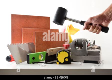 Supply of tools and tiling material on white table and hand with mace and white isolated background. Front view. Stock Photo