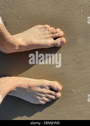 Top view of two men's feet on the sandy beach. Stock Photo