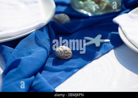 Elegant table setting with blue tablecloth, white plates, seashells, and starfish, creating a sophisticated nautical ambiance Stock Photo