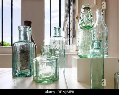 A collection of vintage glass bottles displayed on a sunlit window sill with a view of an urban building exterior in the background Stock Photo