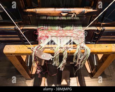 Close-up of a vintage wooden loom showcasing intricate weaving in progress with colorful threads in traditional patterns. Stock Photo